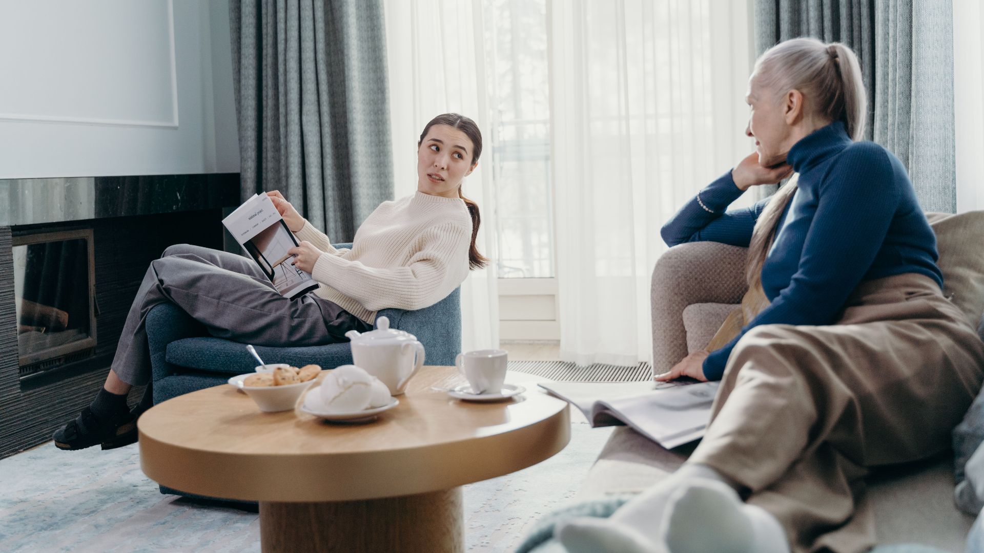 Two women engage in a relaxed conversation in a modern living room setting.
