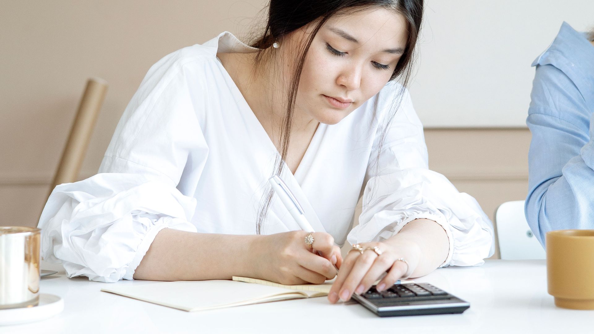 An adult woman attentively doing calculations on a calculator at a desk in a modern office setting.