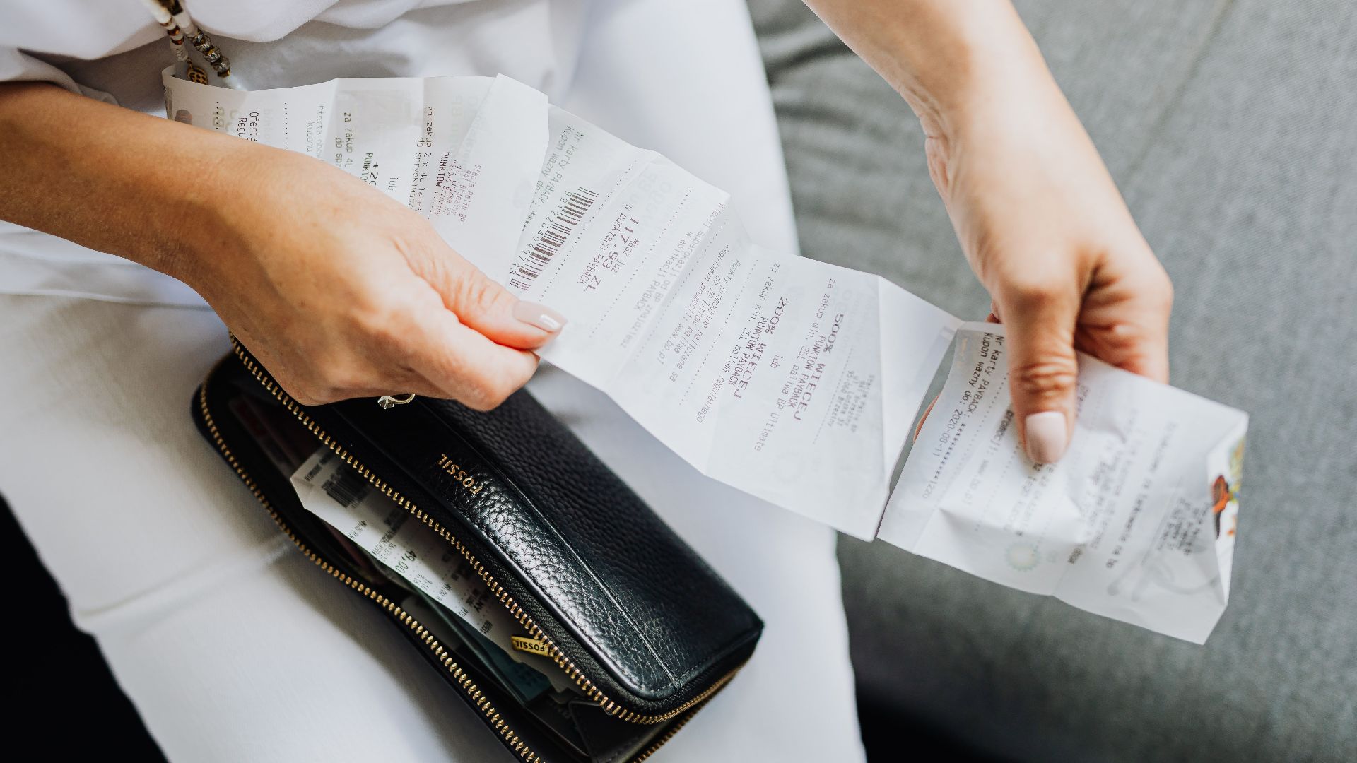Close-up of a woman's hands managing multiple receipts taken from a black wallet.