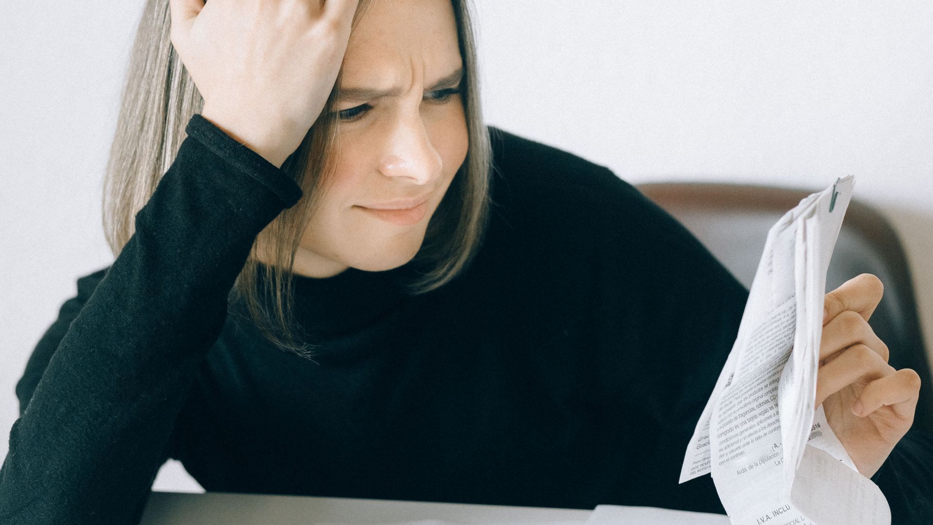 A woman looking concerned while analyzing financial papers at a desk, representing work stress.