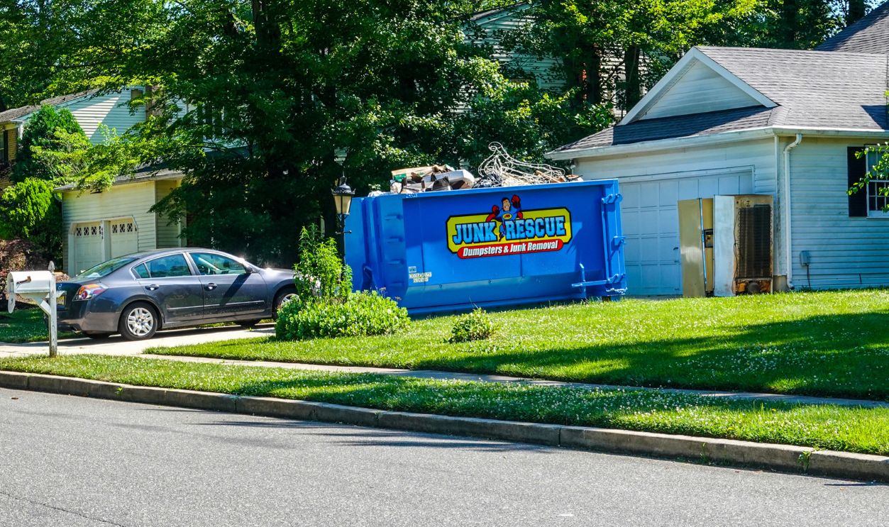 Cherry Hill, New Jersey - August, 2020: A small blue dumpster is seen in the driveway in front of a house. Two refrigerators are in front of the dumpster.