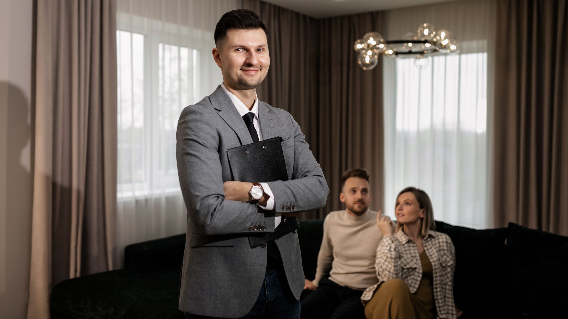 Smiling real estate agent with a clipboard indoors, showing a property to a couple.