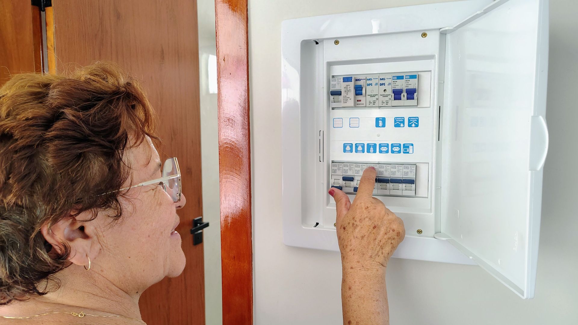 A senior woman is adjusting an electrical fuse panel indoors, demonstrating home safety.
