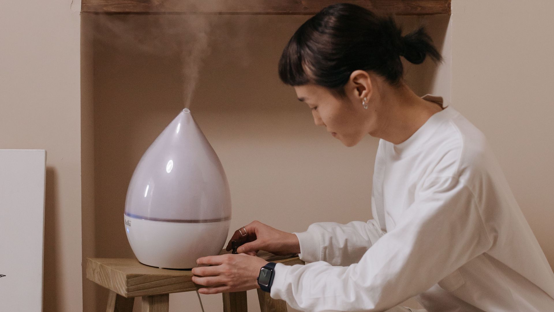 Calm setting with an Asian woman adjusting a humidifier indoors, creating a cozy atmosphere.