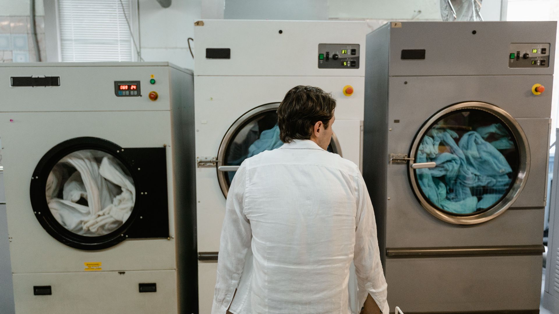 A man uses commercial washing machines at an indoor laundromat.