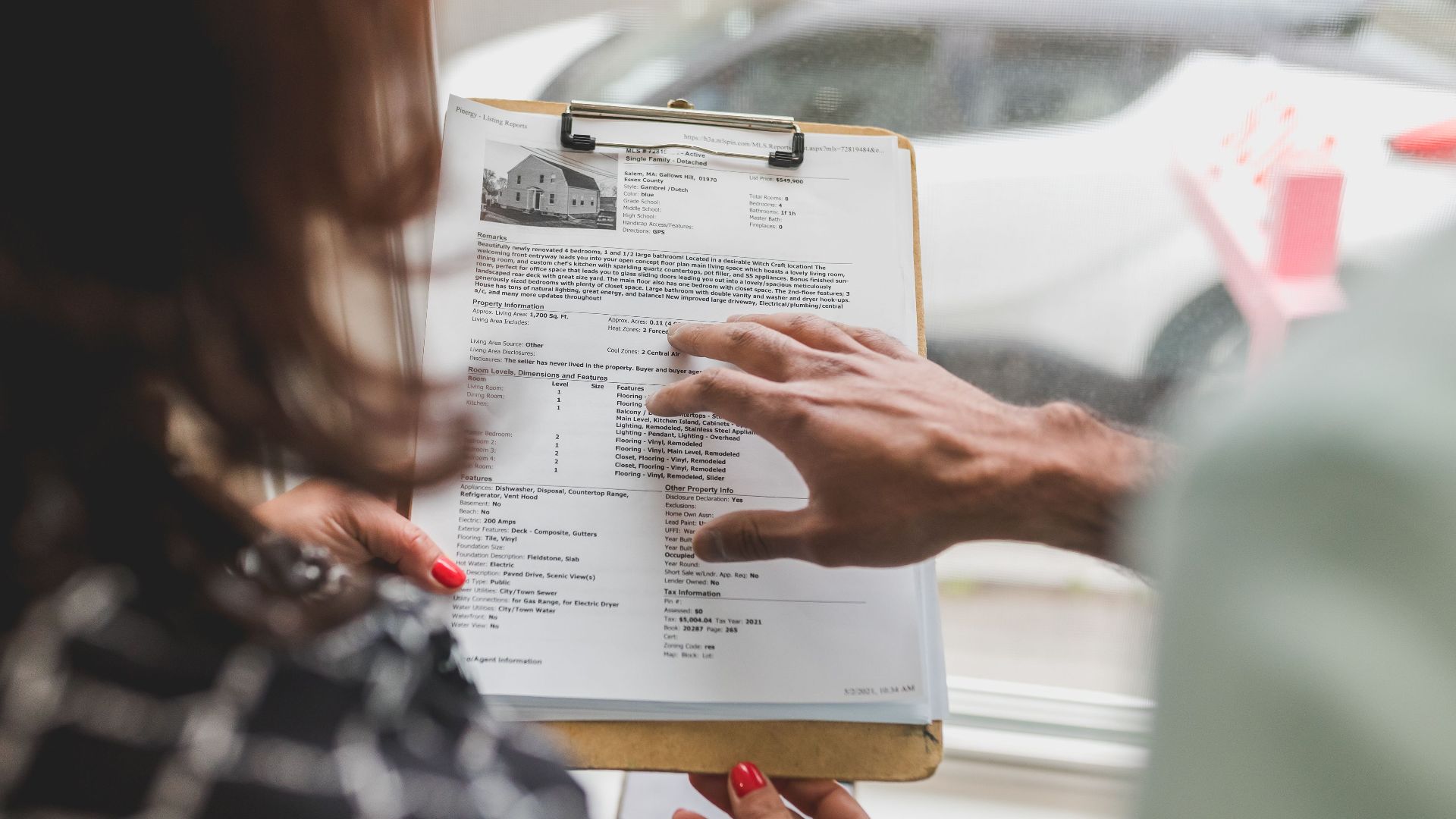 Real estate agent discussing property details with client using a clipboard indoors.