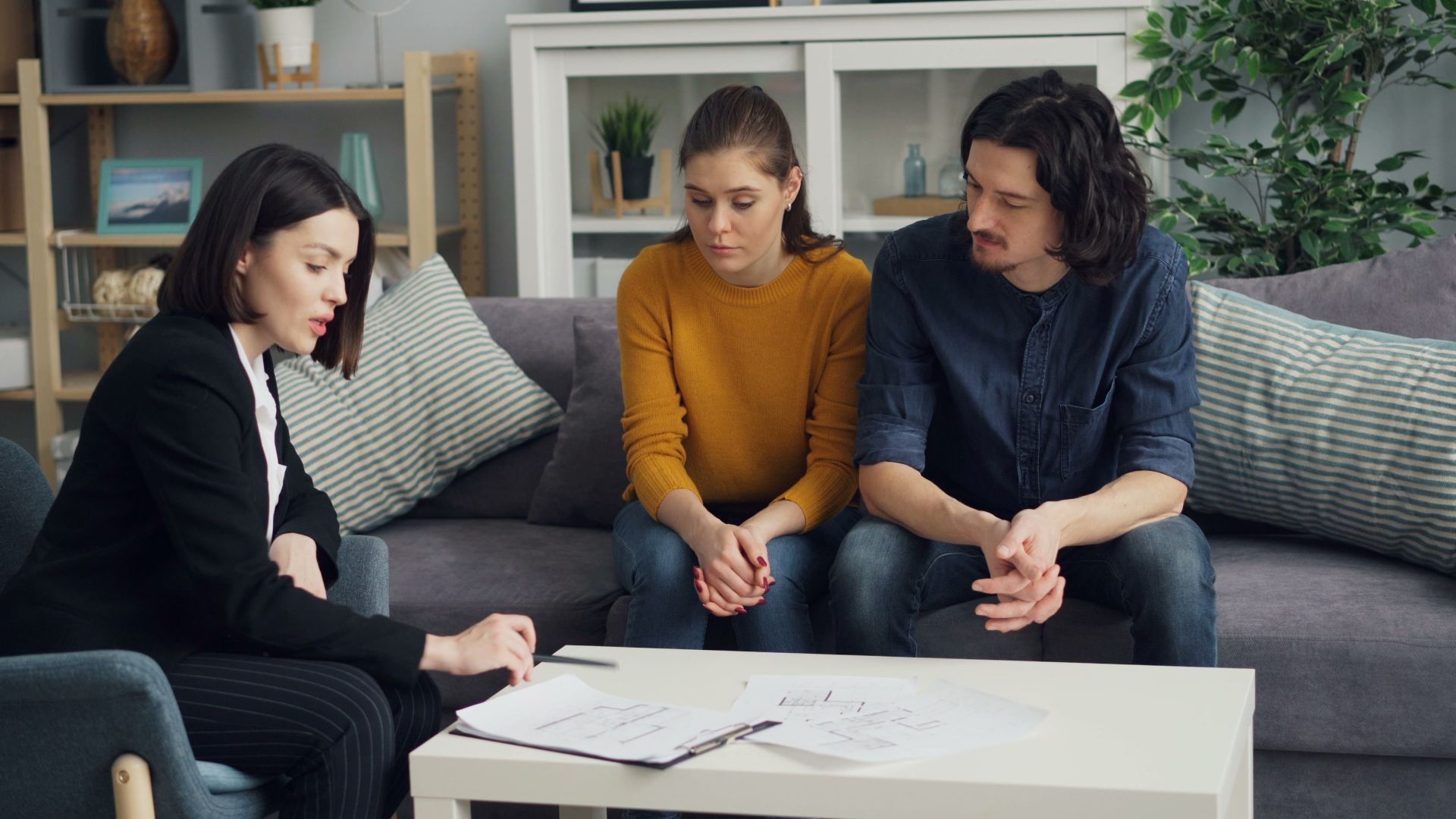 Couple discussing property with real estate agent in cozy living room setting, reviewing documents.