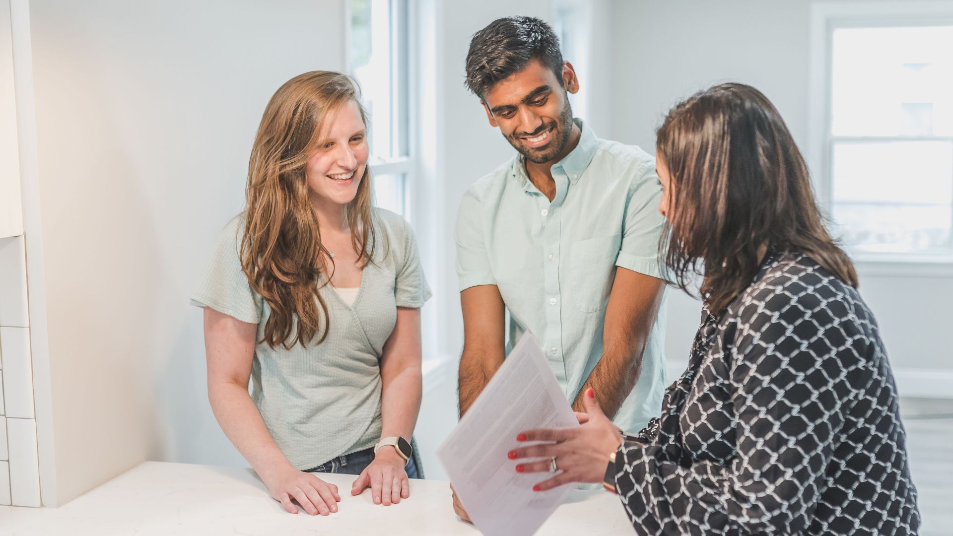 A smiling couple discusses real estate options with an agent inside a modern home.