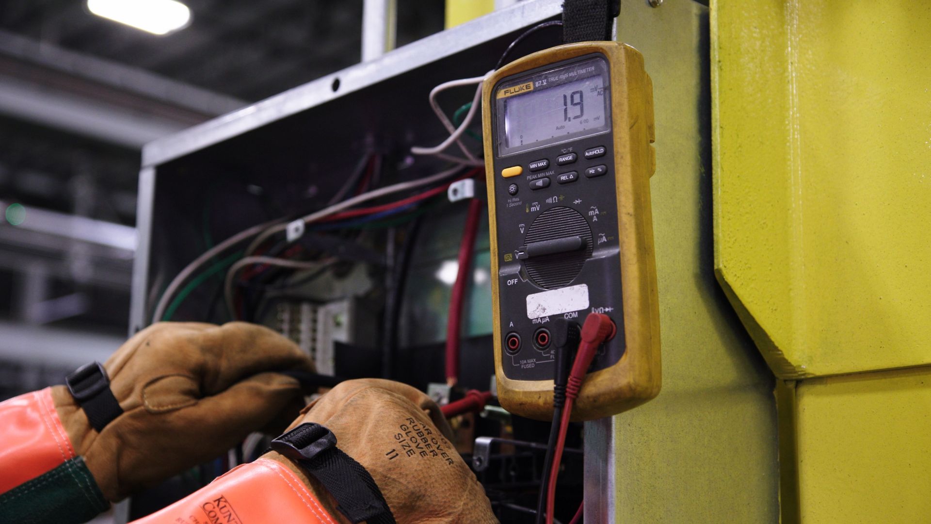 Electrician using a multimeter to fix industrial control panel wiring.