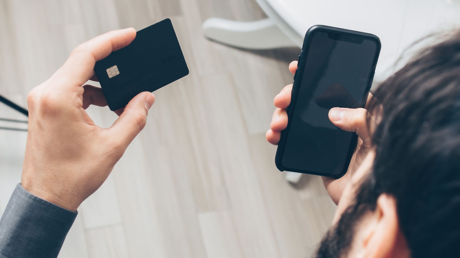 Close-up of man holding a smartphone and credit card, making an online payment indoors.