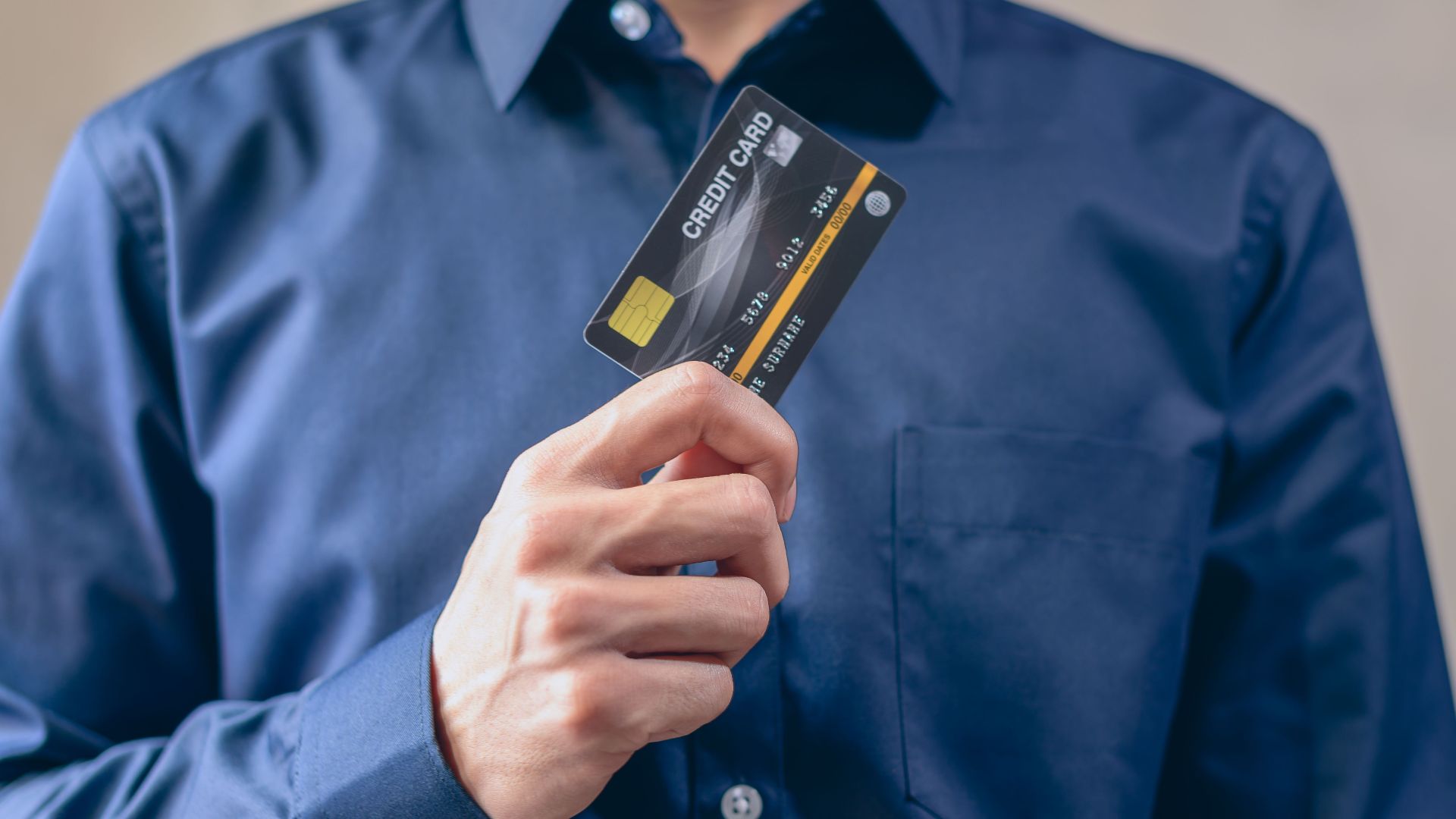 Close-up of a man in a blue shirt holding a credit card, symbolizing finance and security.