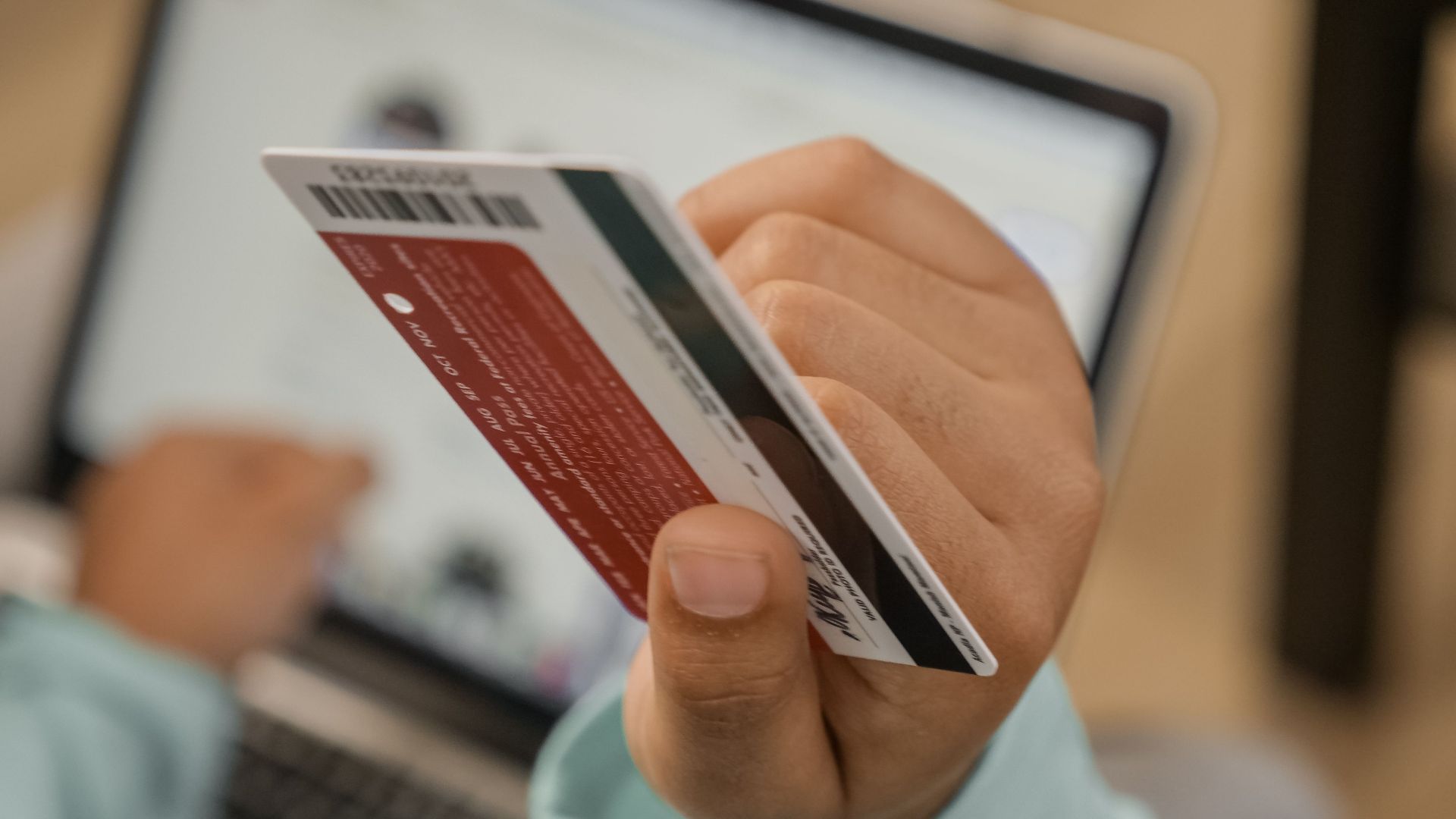 Close-up of hand holding a credit card during an online transaction on a laptop.