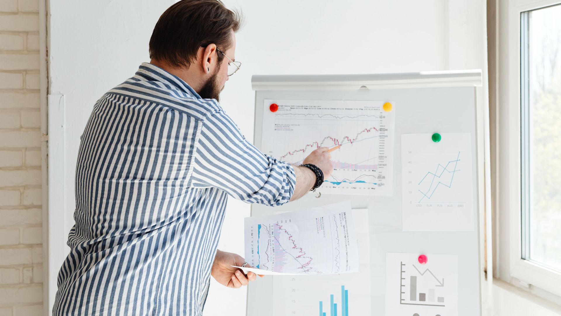 A businessman pointing at financial charts on a whiteboard, discussing stock market trends.