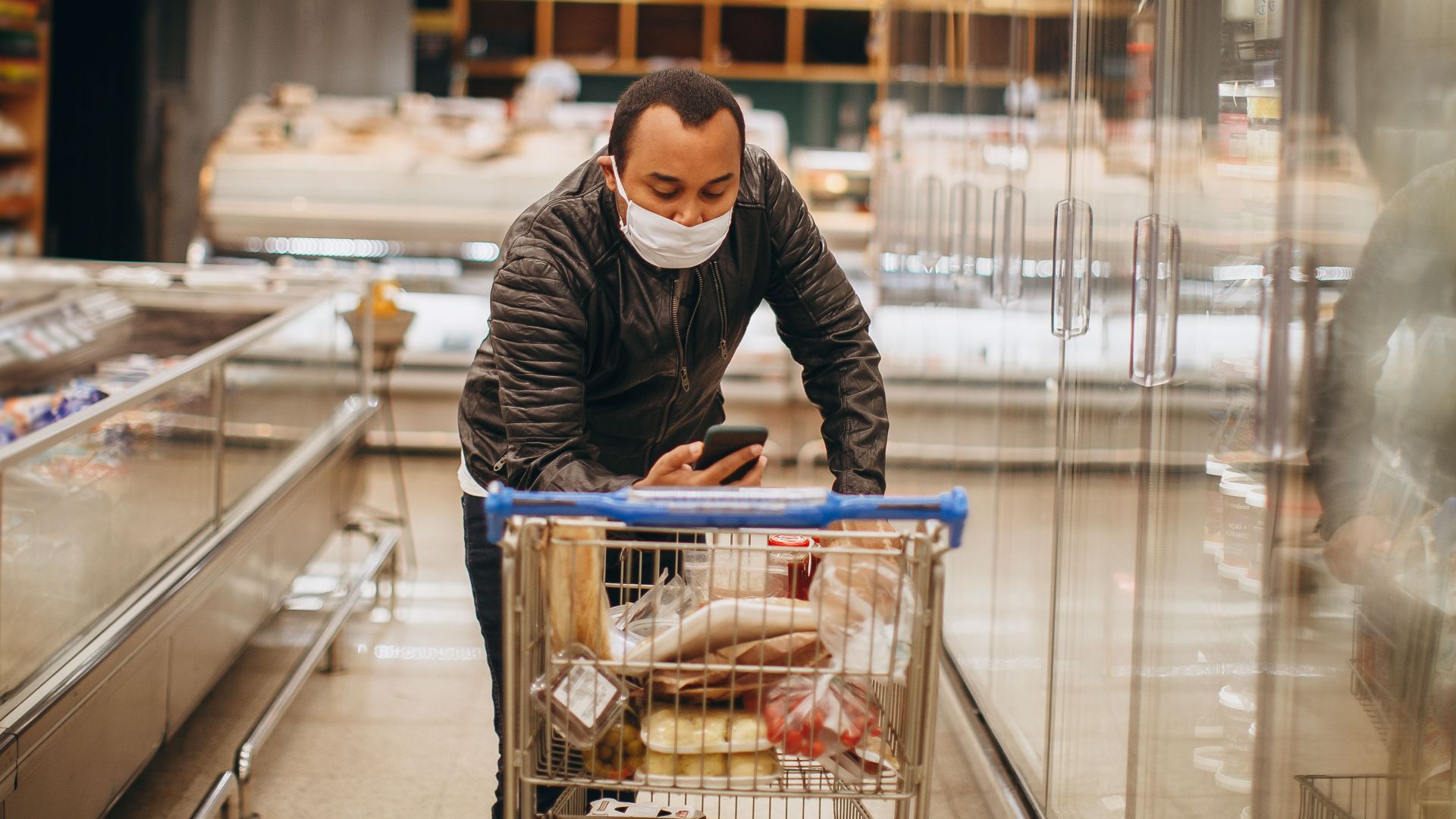 Man wearing mask shops in a supermarket, pushing a cart in the aisle.