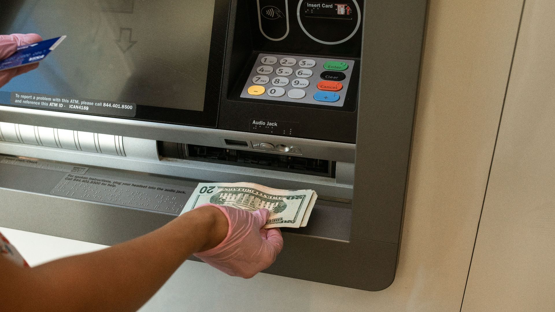 A person wearing gloves withdrawing cash from an ATM machine showcasing money handling and hygiene.