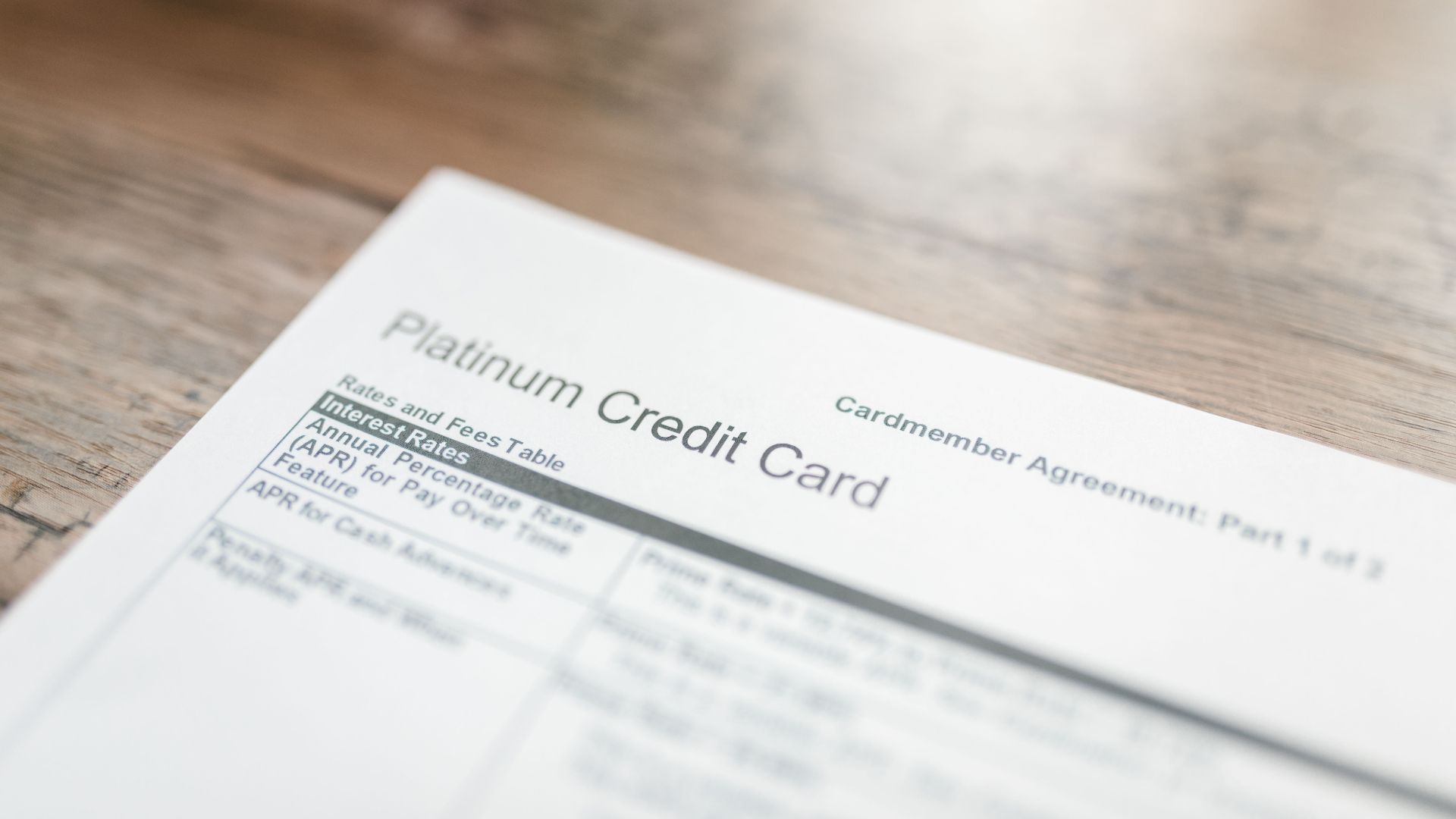 Close-up of a platinum credit card document with interest rates table on a wooden surface.