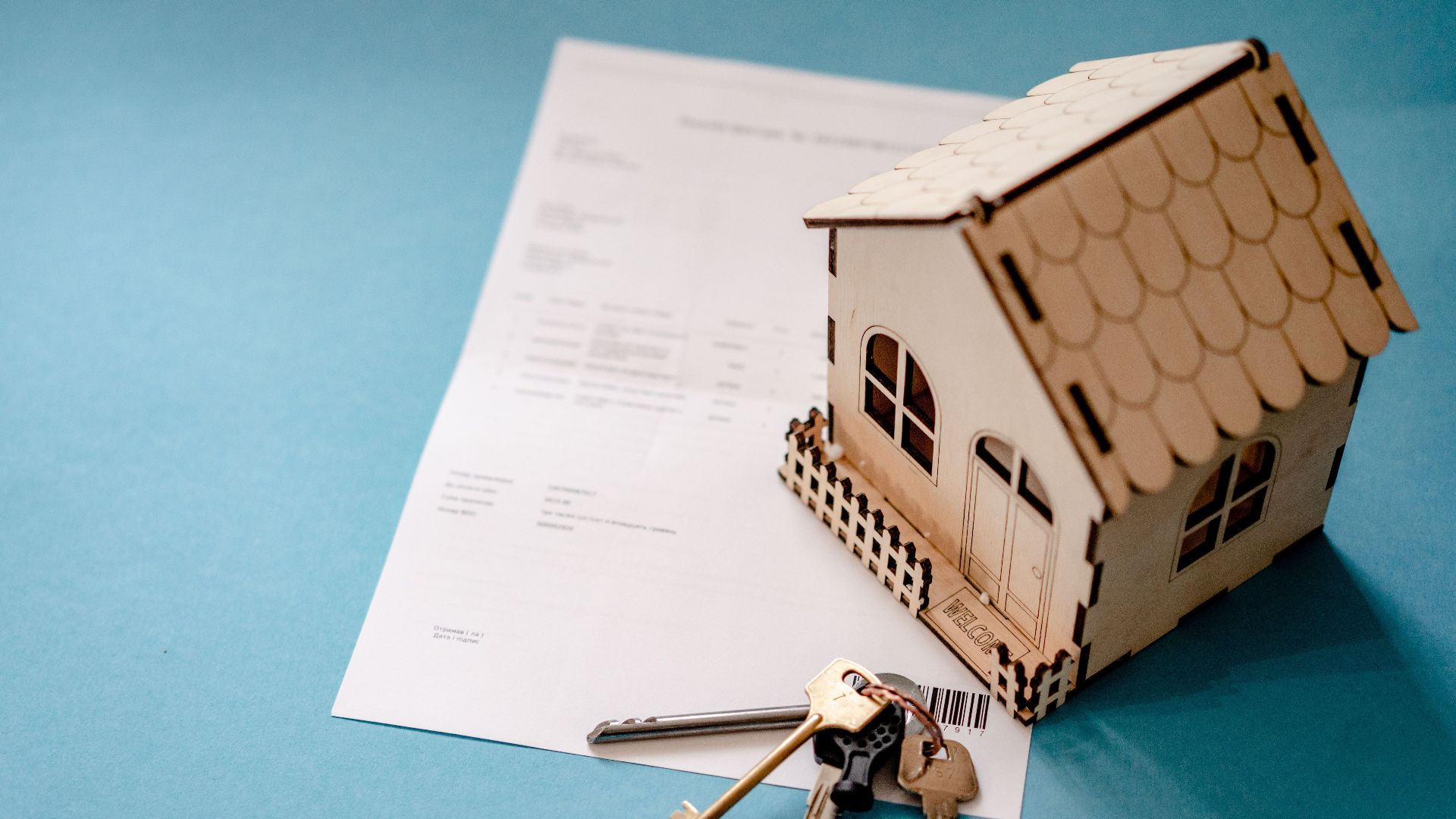 Miniature wooden house with keys and contract symbolizing real estate transactions.