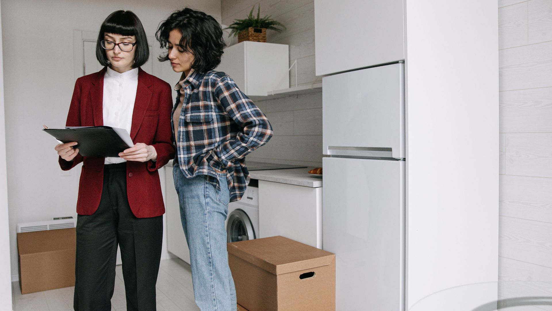 Two women reviewing documents in a kitchen amid moving boxes.
