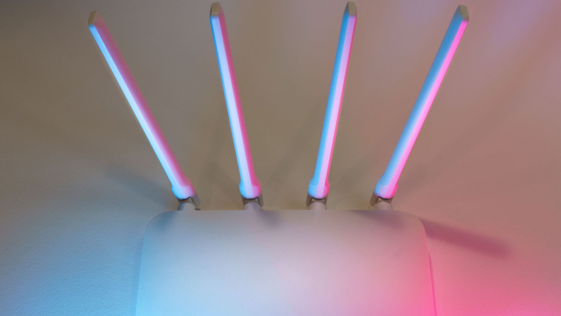 Sleek white wireless router with four antennas emitting soft blue and pink light.