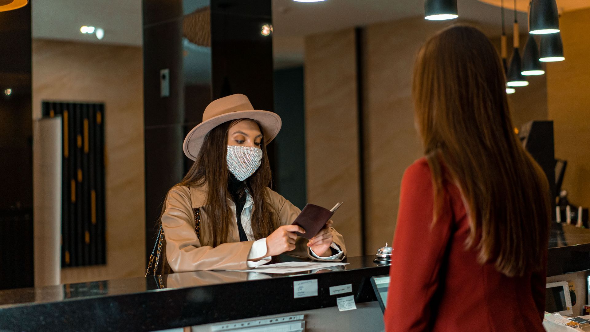 A woman wearing a mask checks in at a hotel reception desk.