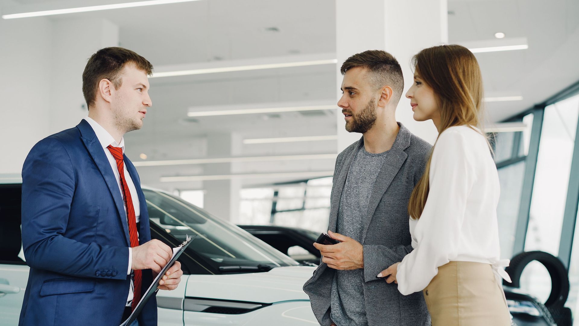 Car salesman assisting a couple in a modern showroom with a luxury car.