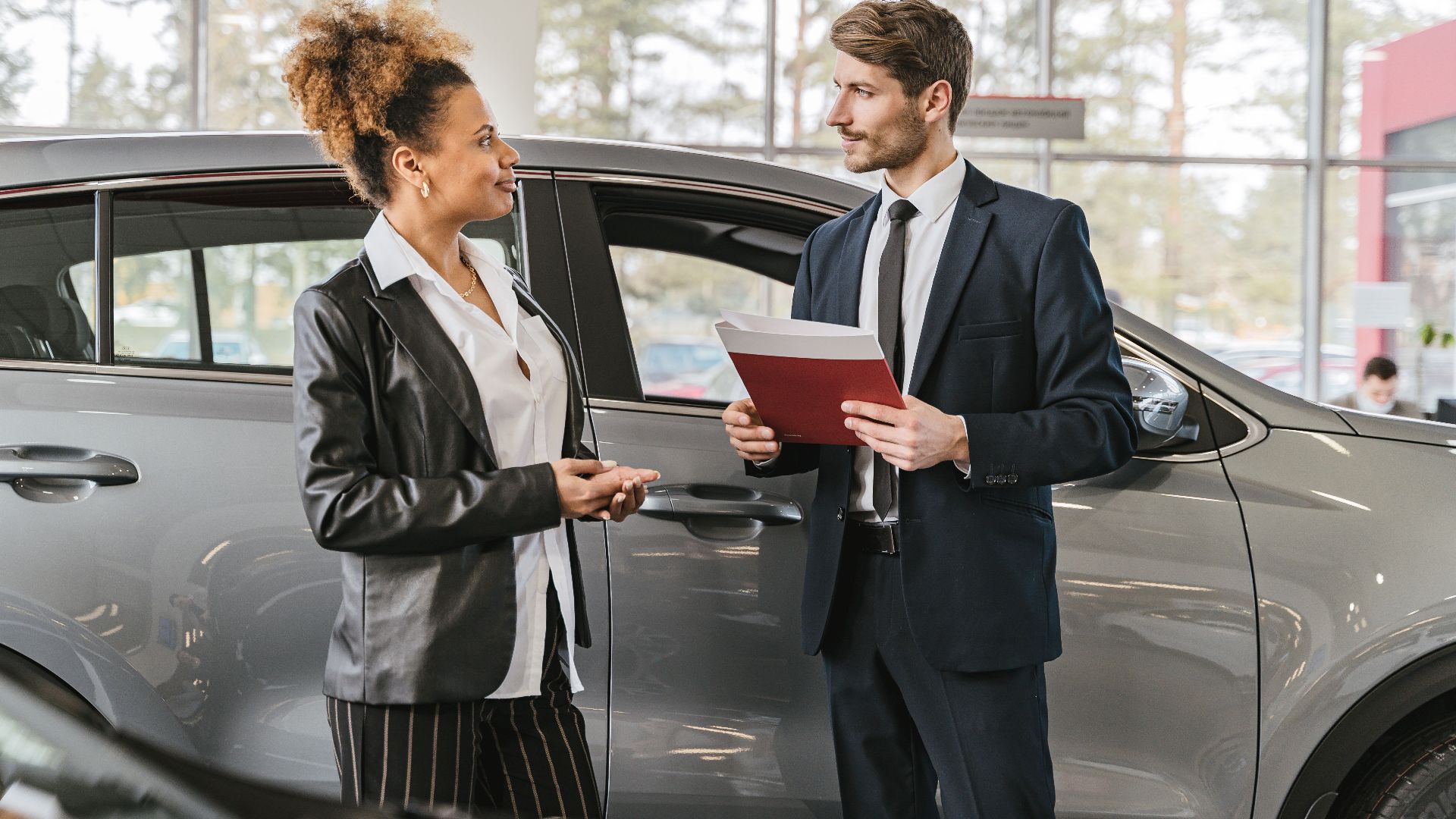 A woman discussing car purchase with a dealer inside a car dealership showroom.