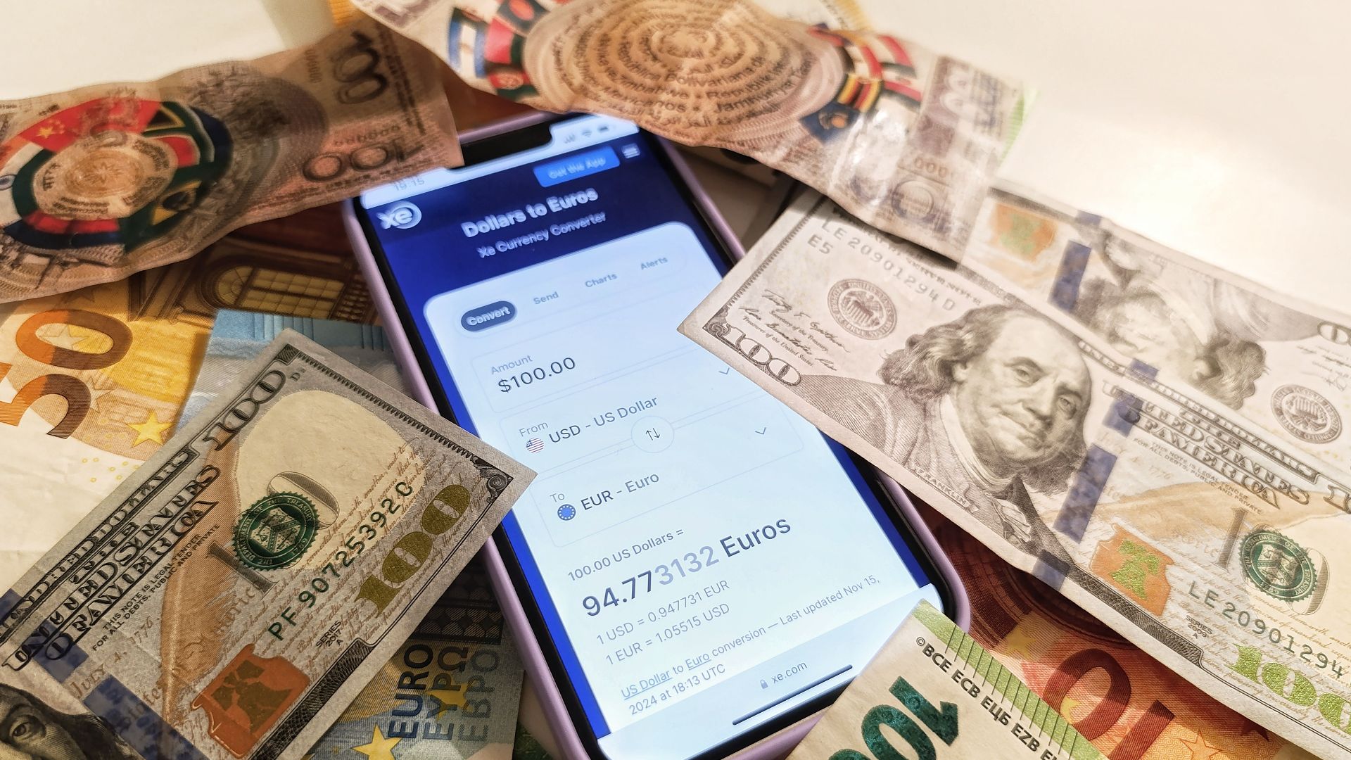 A smartphone displaying a currency converter surrounded by dollar and euro banknotes, highlighting exchange rates.