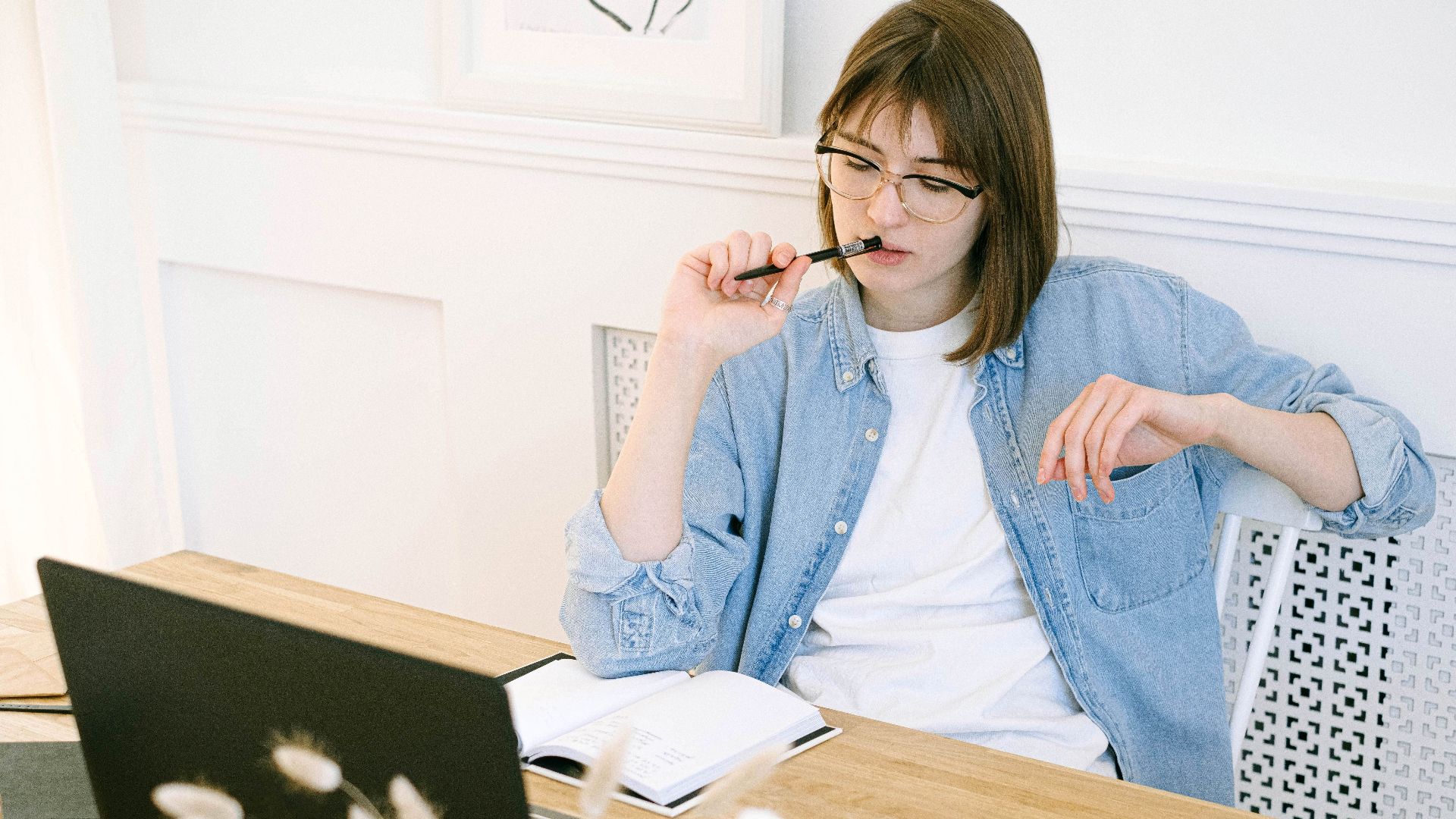 Woman working thoughtfully in home office, reflecting on ideas with laptop and notebook.