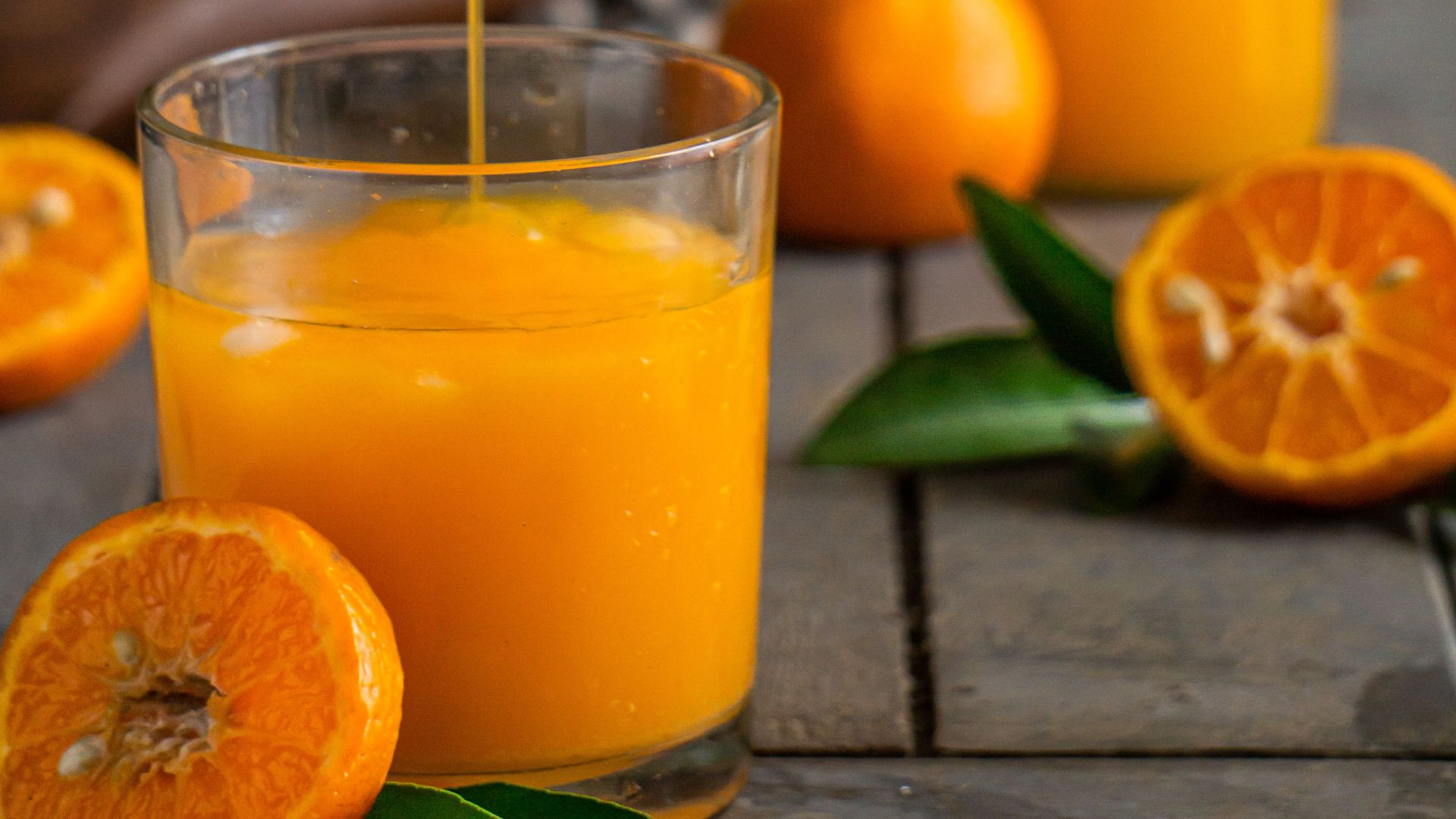 Vibrant orange juice being poured into a glass surrounded by fresh oranges, highlighting freshness and health.