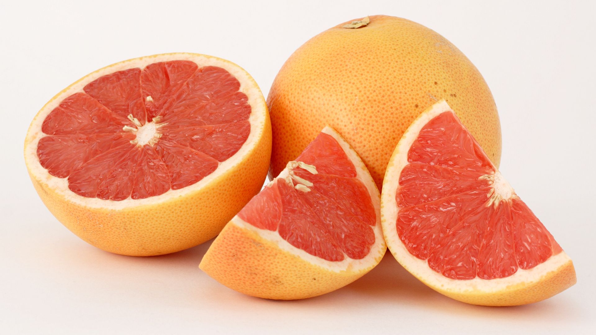 This photograph shows two pink grapefruits (Citrus ×paradisi), one of the two cut in pieces.