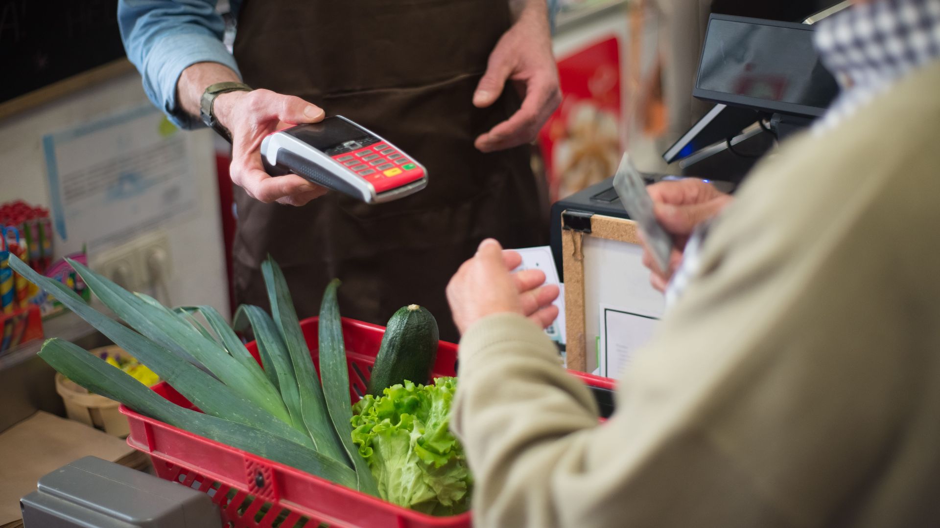 Close-up of customer paying for groceries with produce at a store checkout counter.