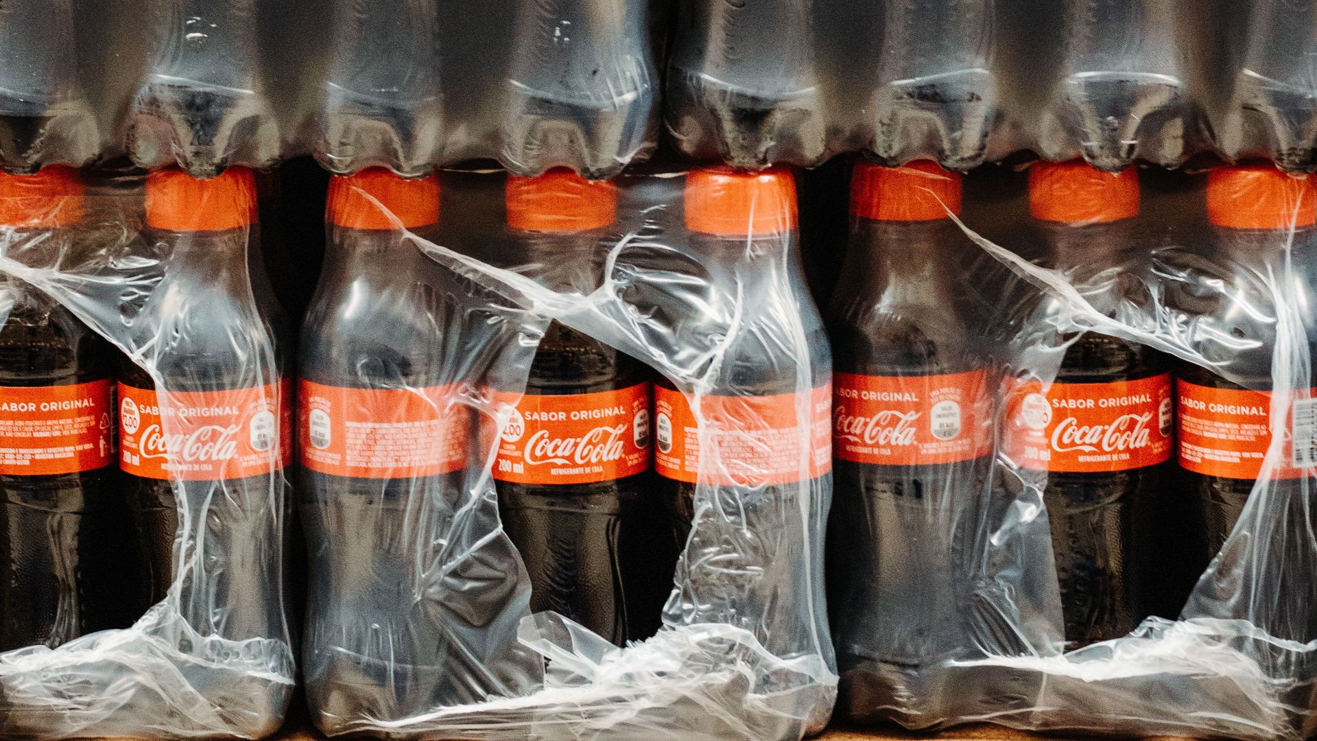 Vertical shot of stacked Coca Cola bottles wrapped in plastic packaging.
