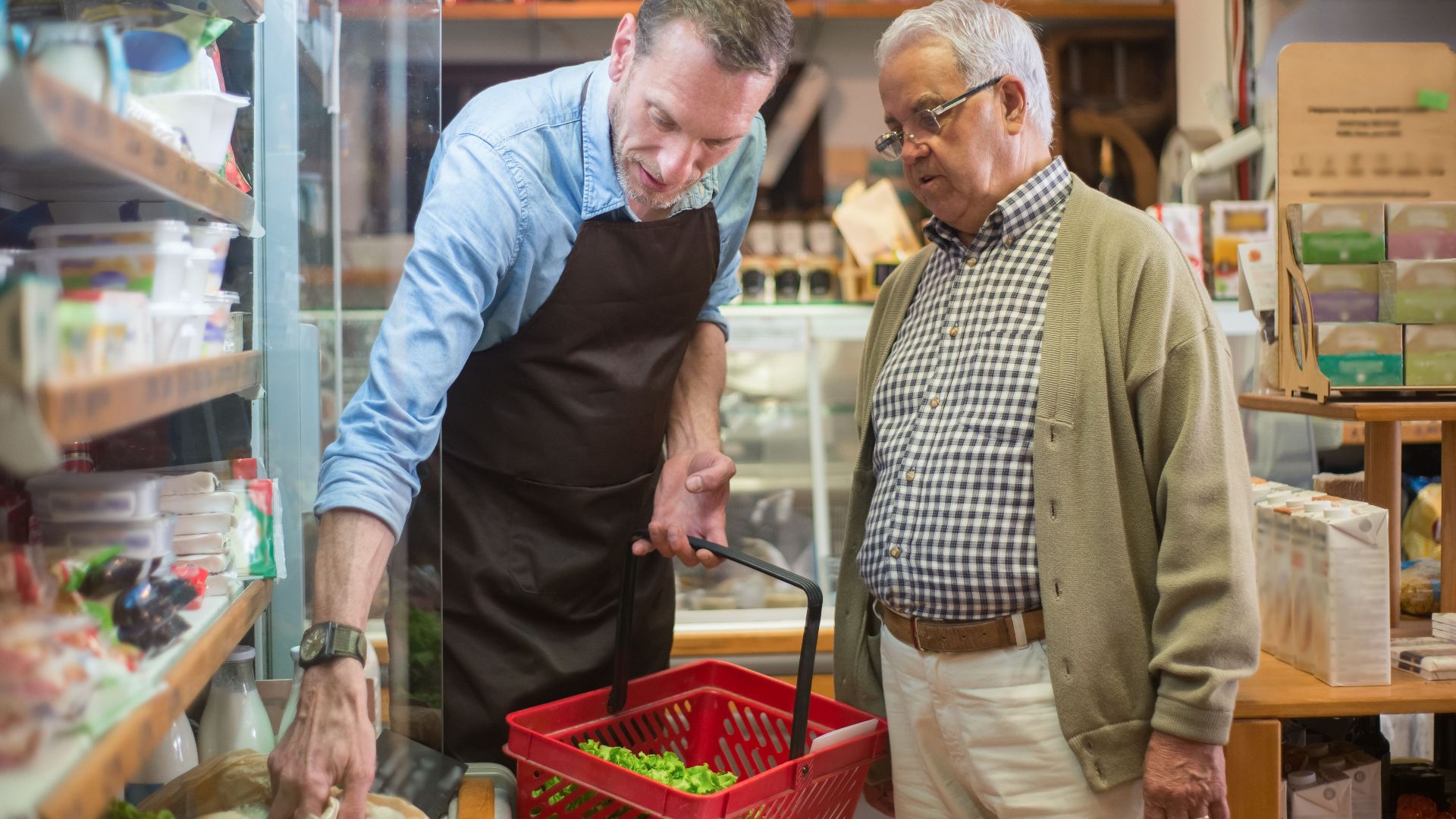 A salesman helps an elderly man with shopping in a local grocery store.