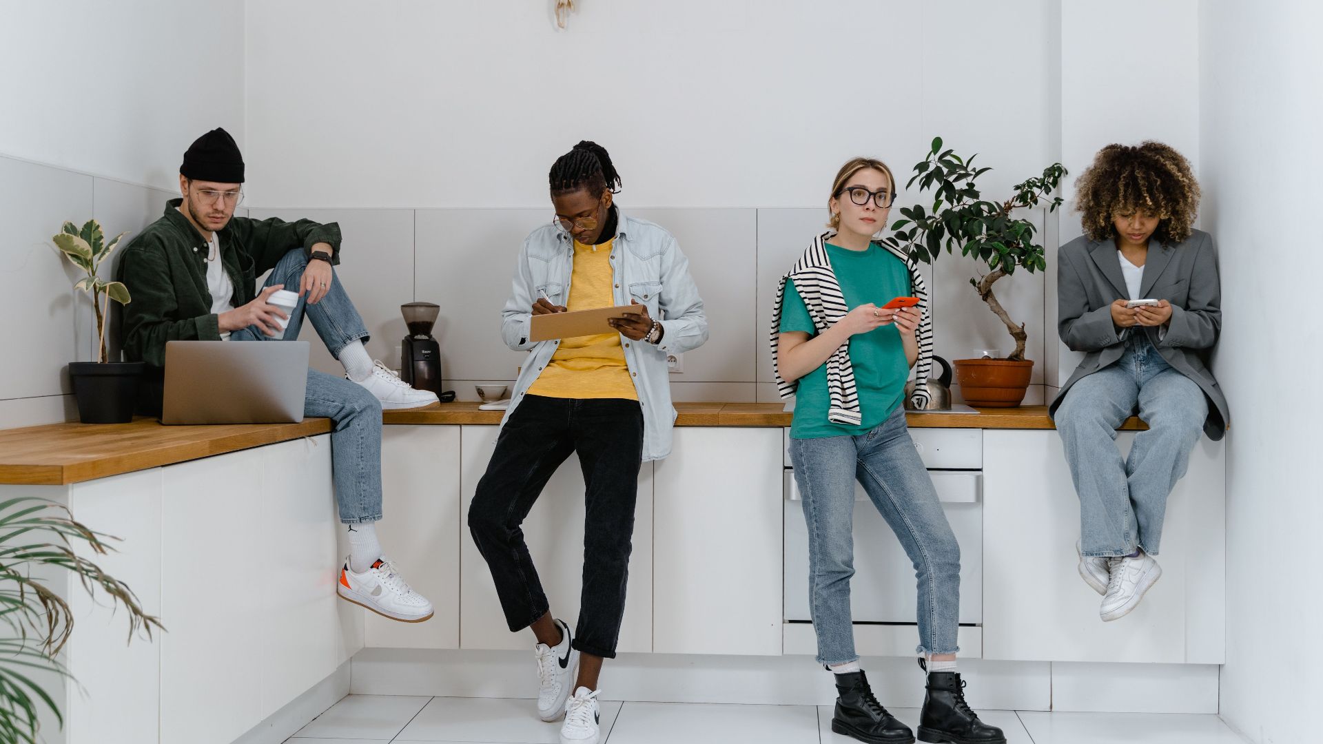 Casual and diverse colleagues using gadgets in a modern office kitchen area.