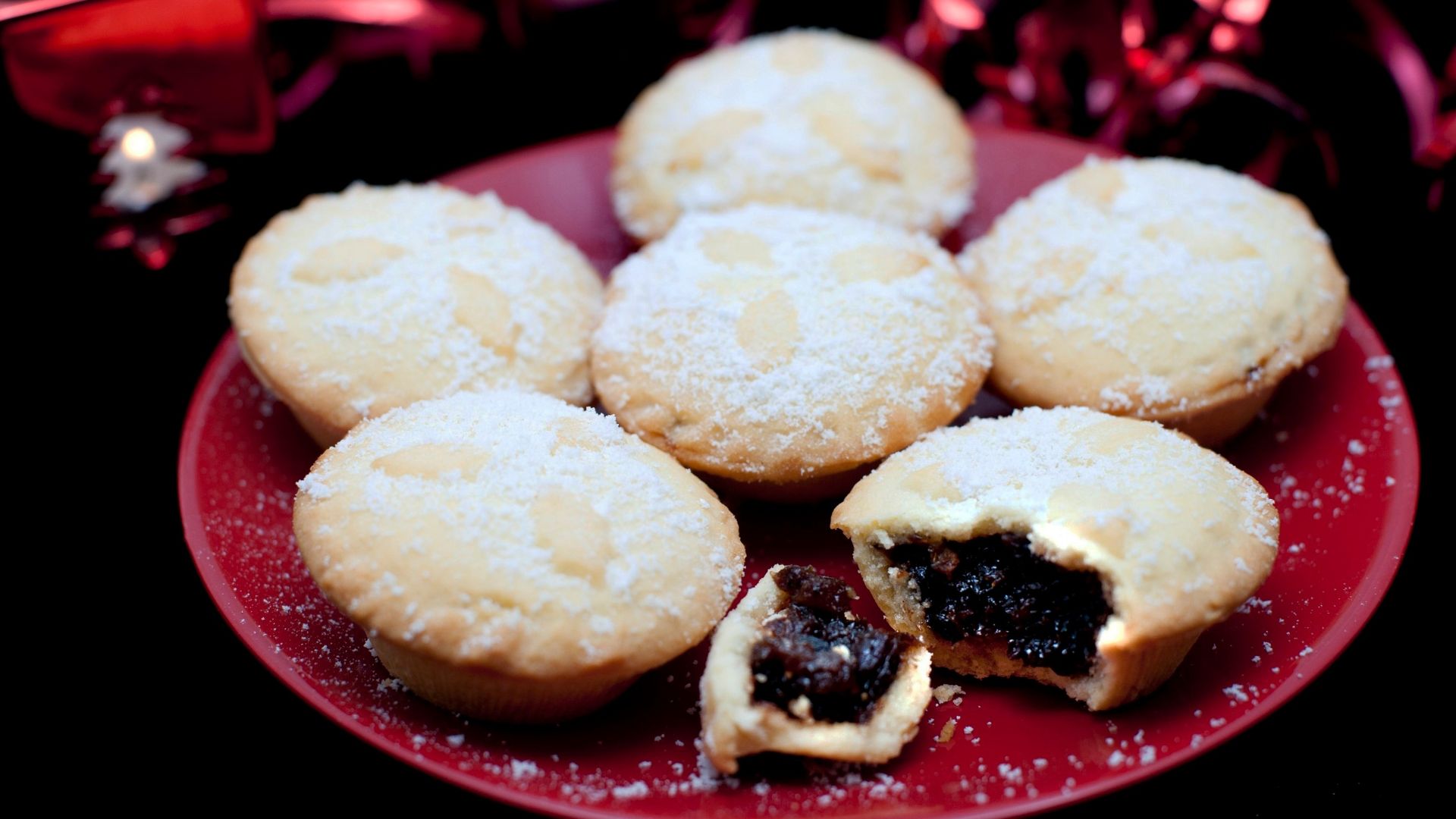 Plate of freshly baked festive Christmas mince pies with decorated golden crusts and spicy fruit filling served sprinkled with sugar, one broken open to reveal the filling