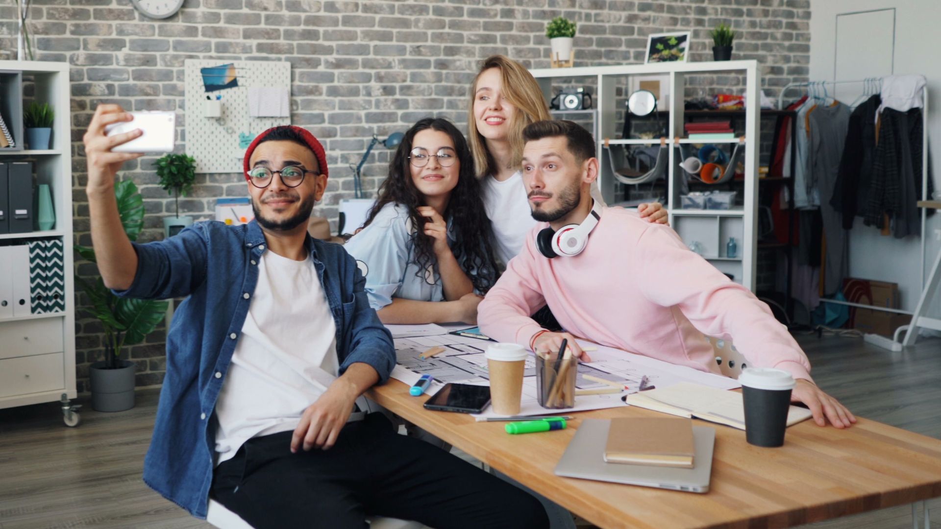 A diverse group of young professionals take a fun selfie in a trendy office space.