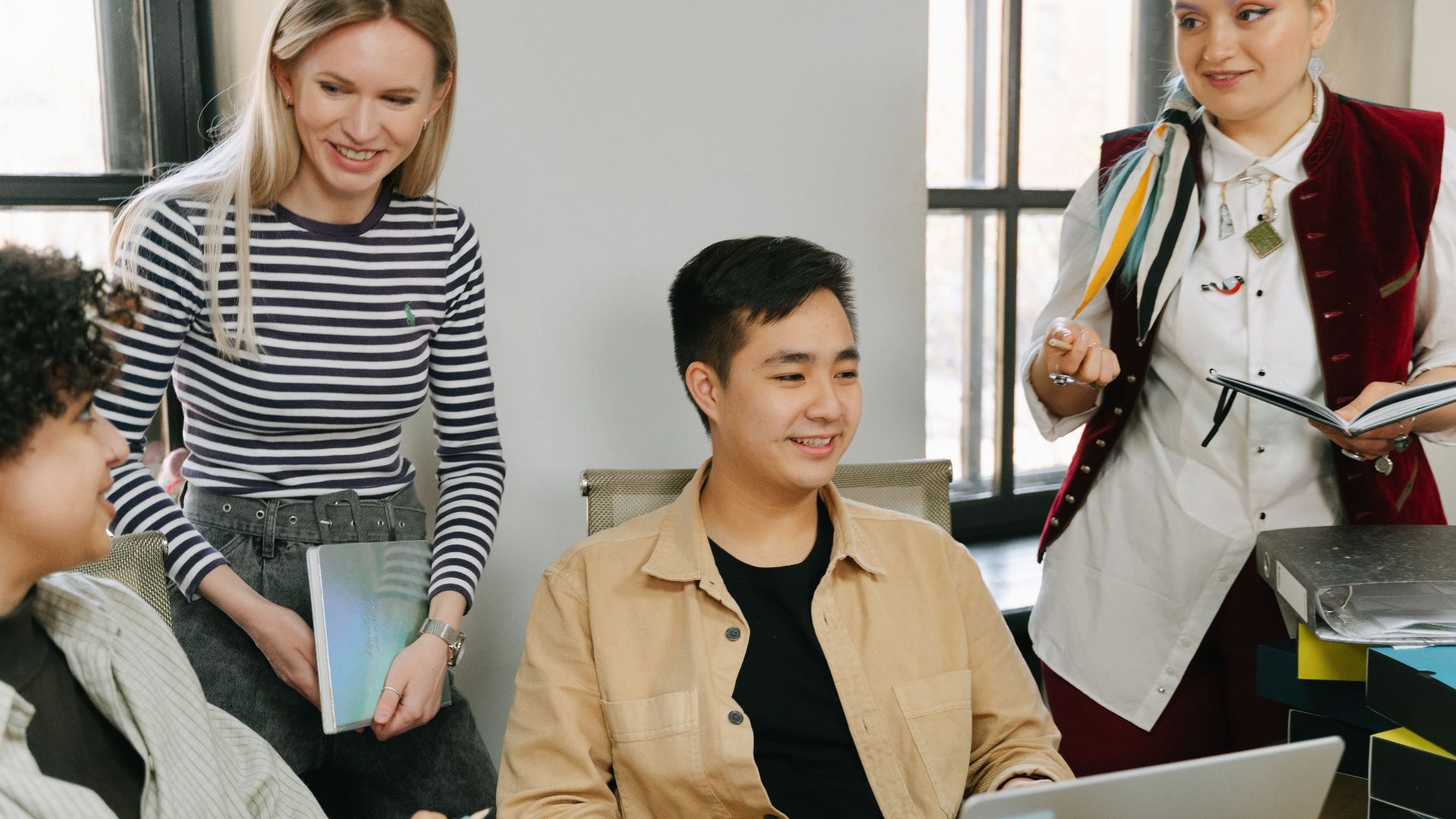A diverse group of young professionals collaborating in a modern office setting, engaging in teamwork and discussion.