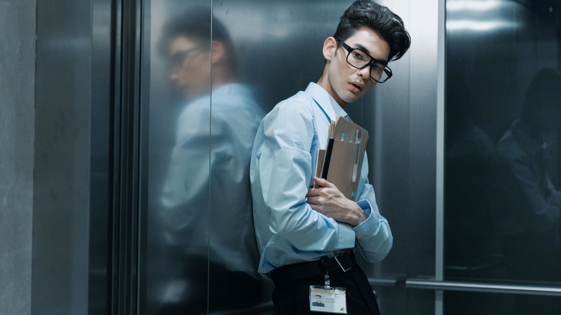 Asian man in a professional attire holding folders and pens in an elevator.