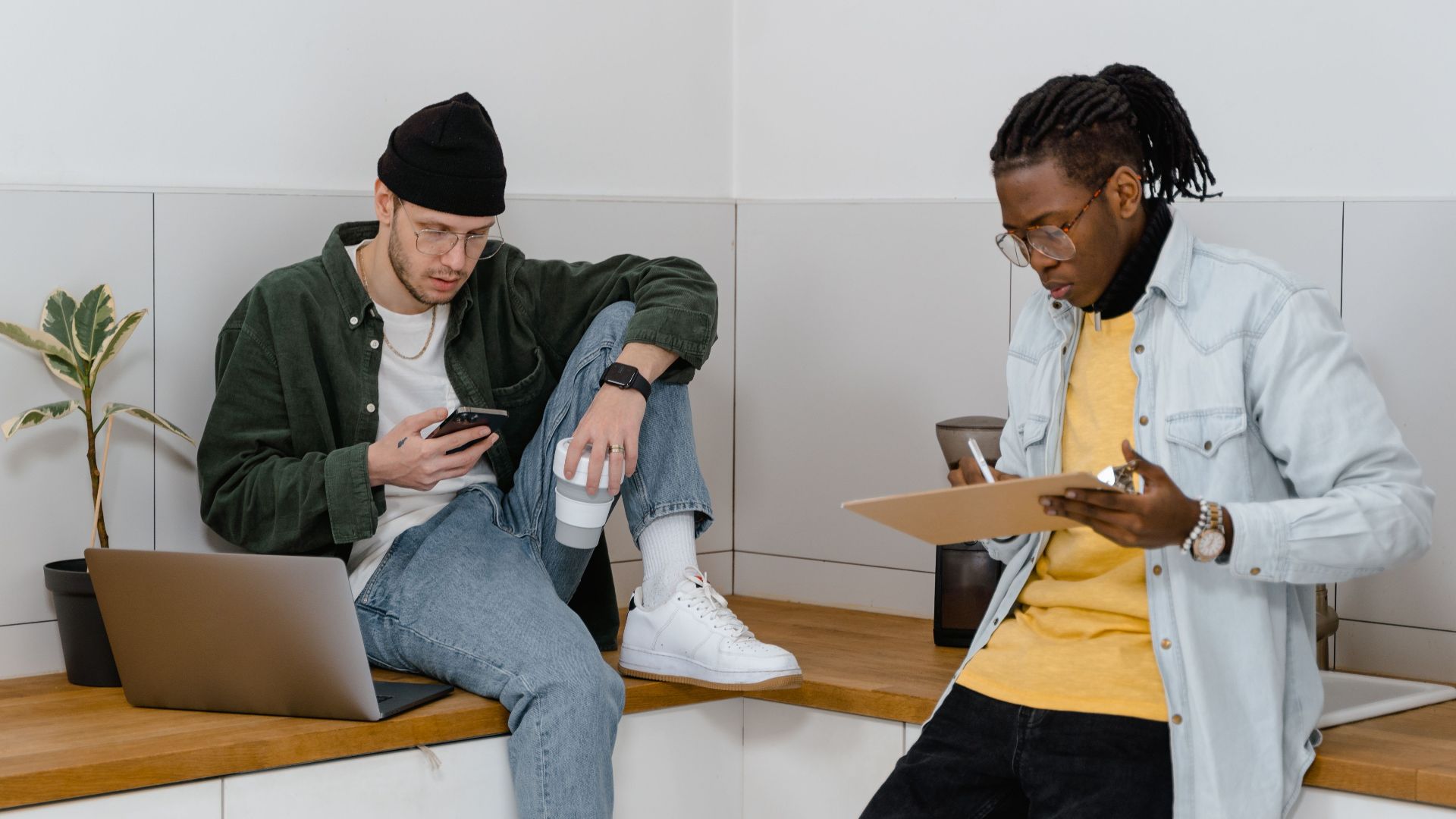 Two men collaborating in a modern kitchen setting, using laptops and smartphones.