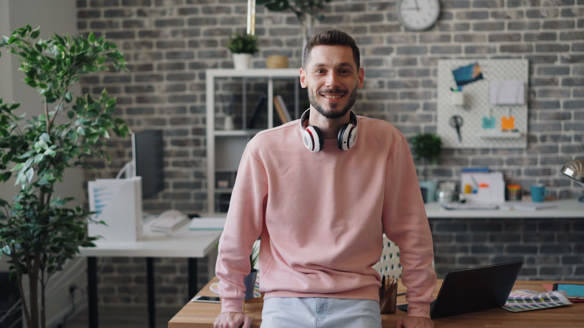 Casual dressed man smiling with headphones in a modern office setting, showcasing a relaxed work environment.