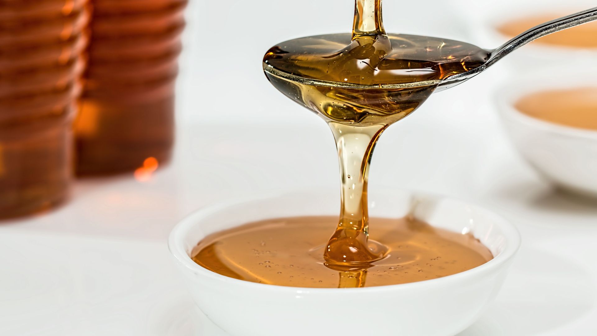 Delicious honey pouring slowly from a spoon into a white bowl, highlighting its golden hue and viscosity.