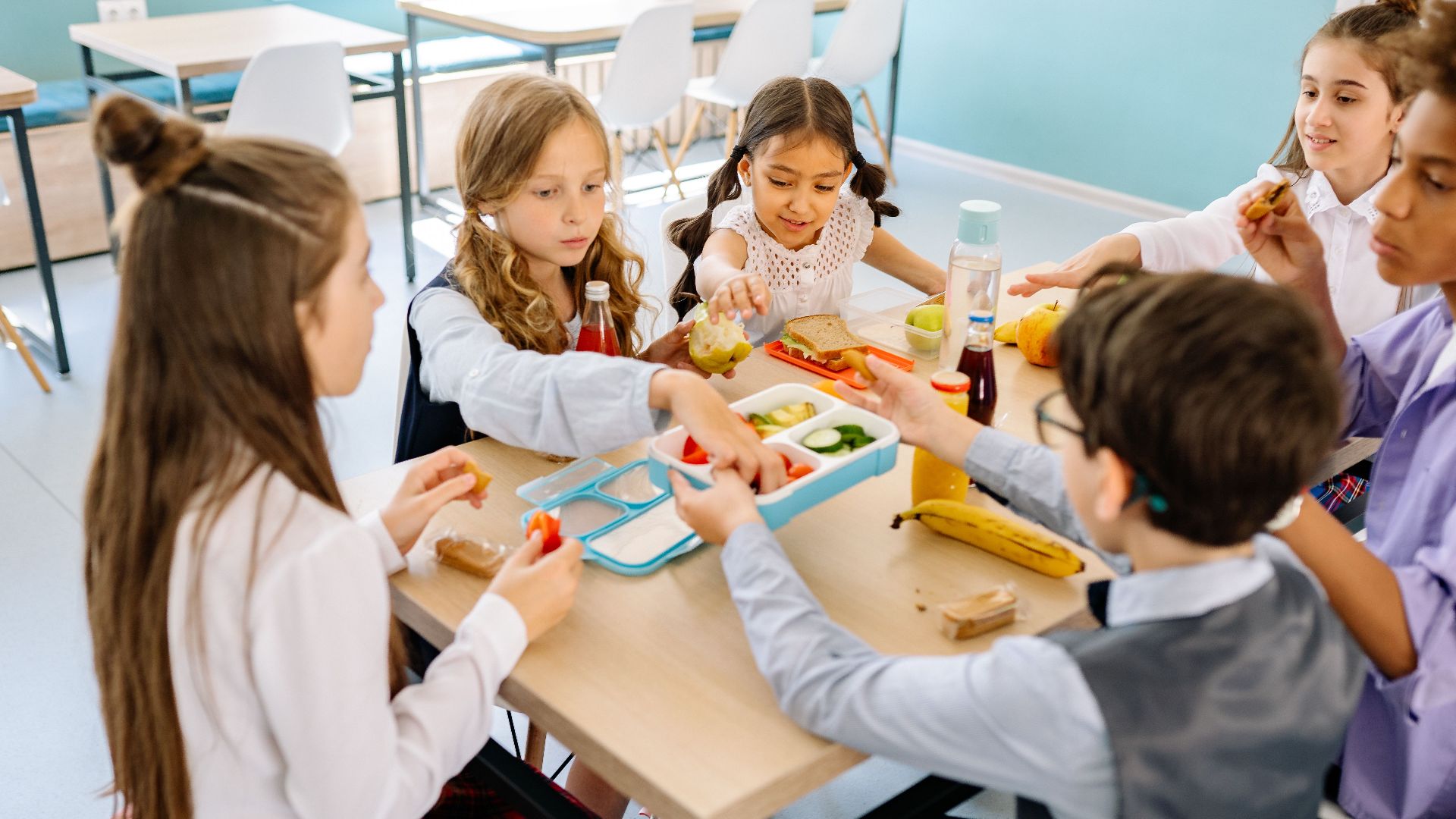 Group of diverse children having lunch in a school canteen, sharing and enjoying healthy snacks.