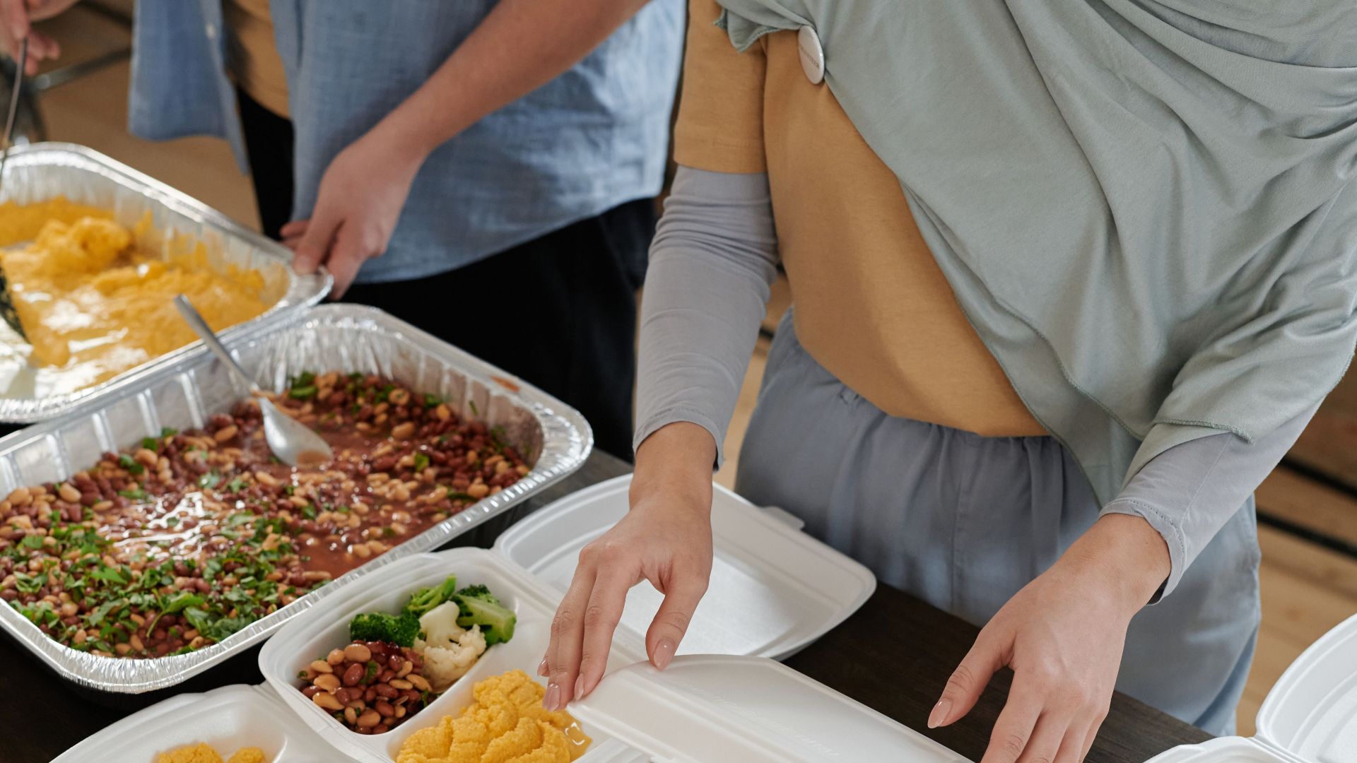 Preparing various lunch boxes with vegetables, beans, and hummus for meal distribution.