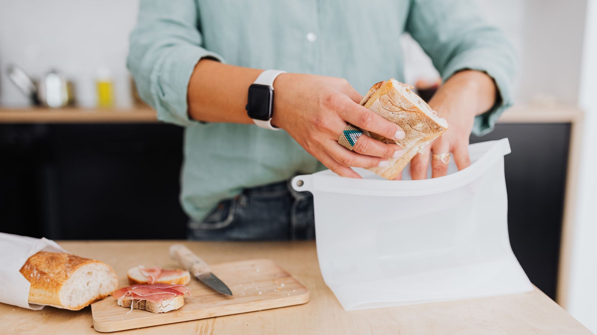 A person packs a sandwich into a silicone bag on a kitchen counter, highlighting eco-friendly food storage.