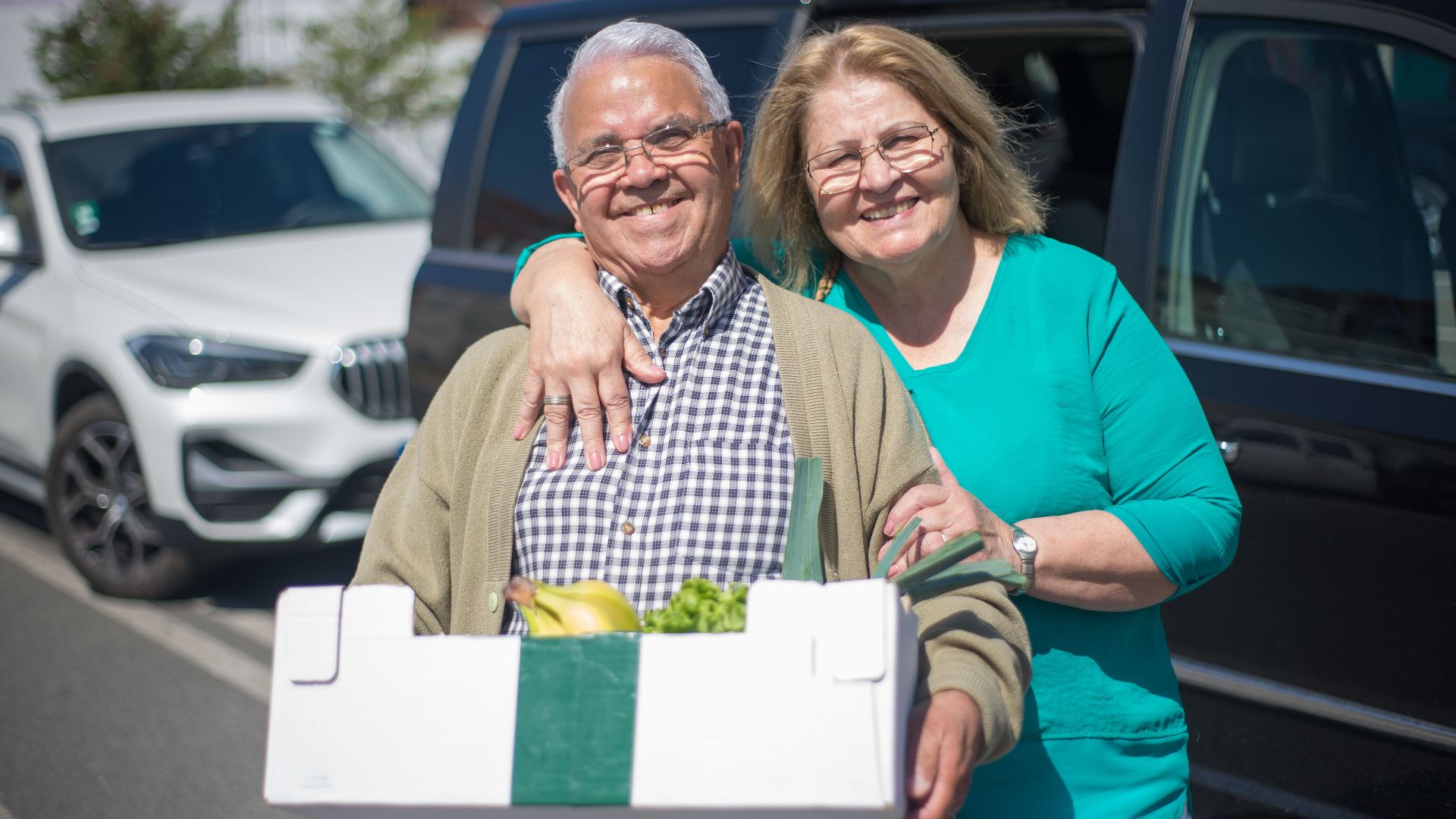 Elderly couple happily shopping with a grocery box outdoors in Portugal.