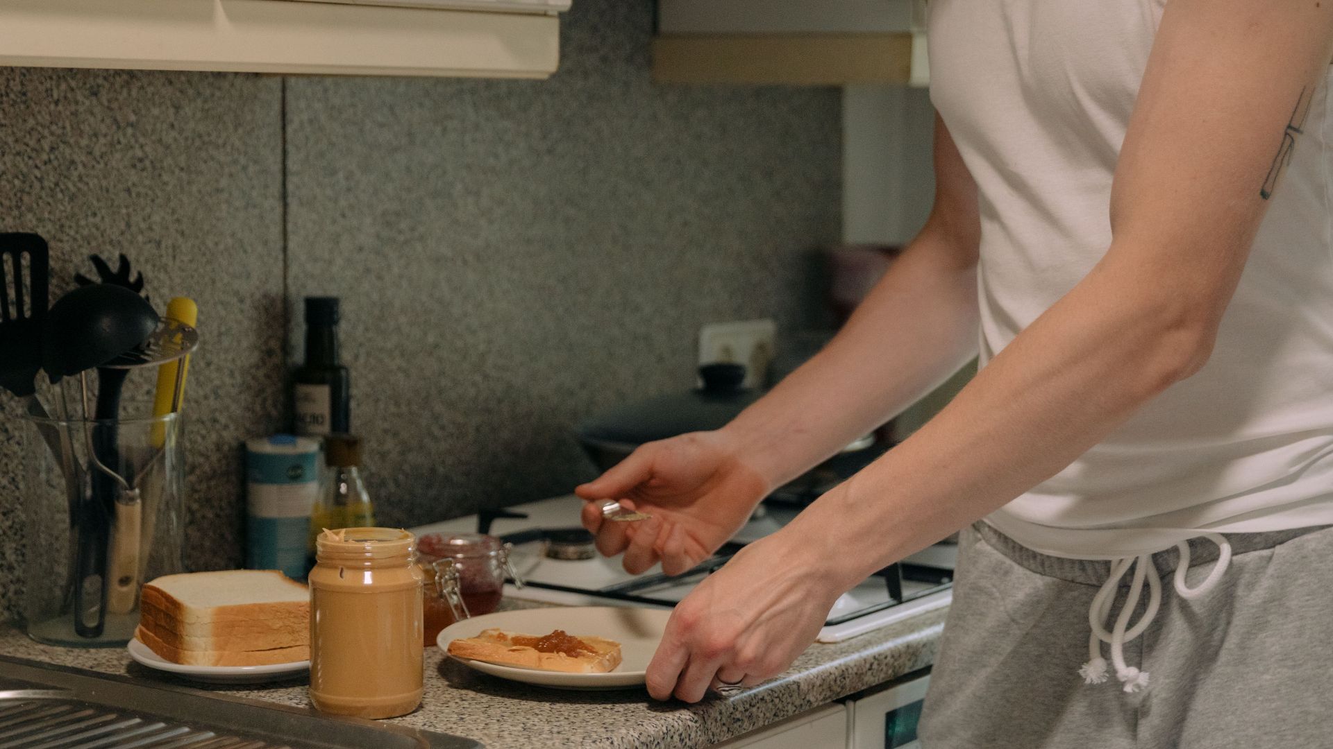 A person prepares a classic peanut butter and jelly sandwich on a kitchen counter.