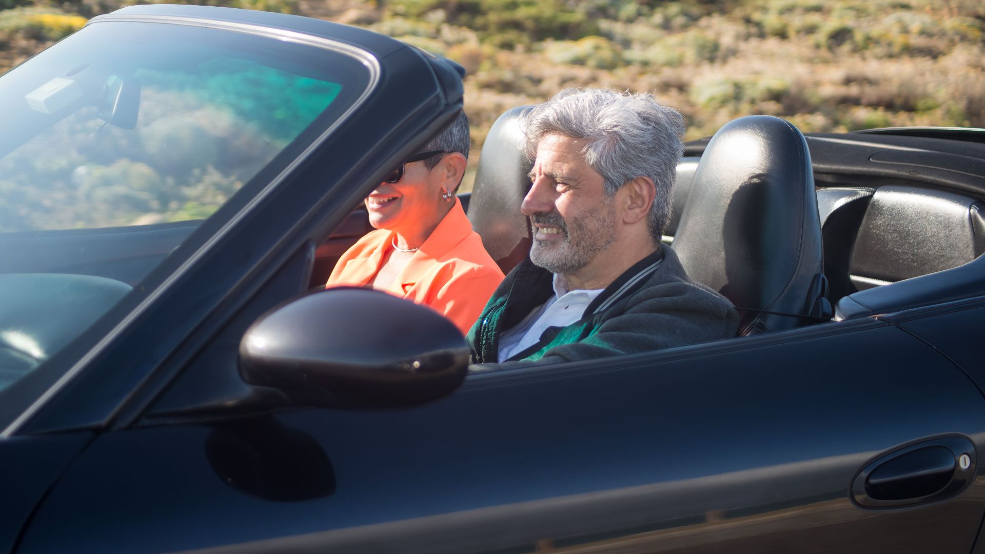 Happy senior couple driving a luxury convertible car on a sunny day outdoors in Portugal.