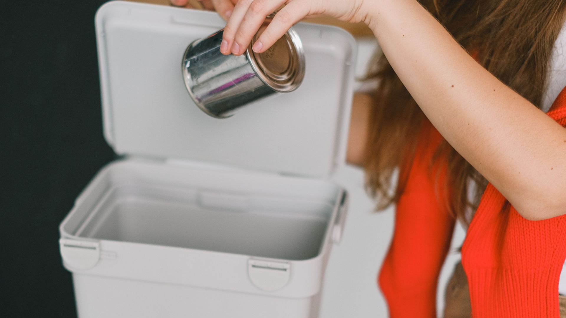 From above of crop anonymous female doing household chore and sorting trash for recycling while putting tin can in container with inscription metal