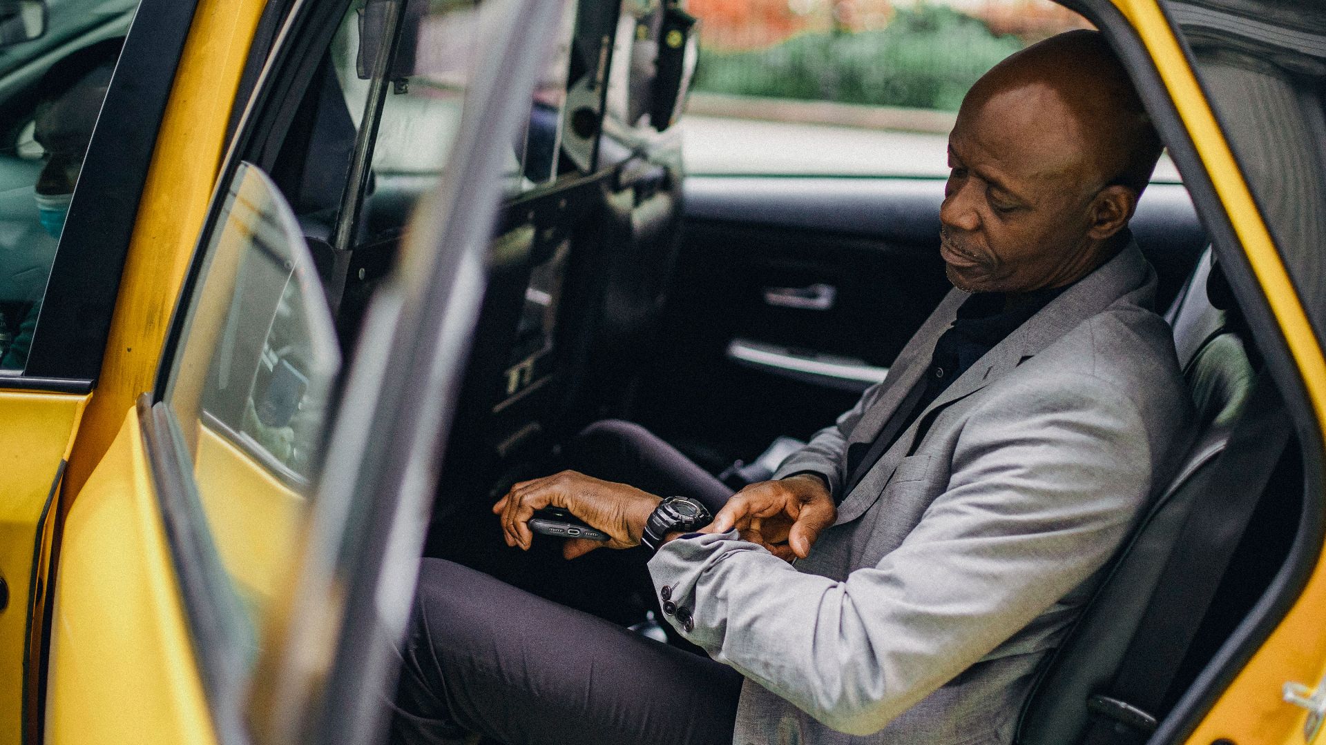 Side view punctual African American male wearing formal suit sitting in taxi back seat and checking time on wristwatch