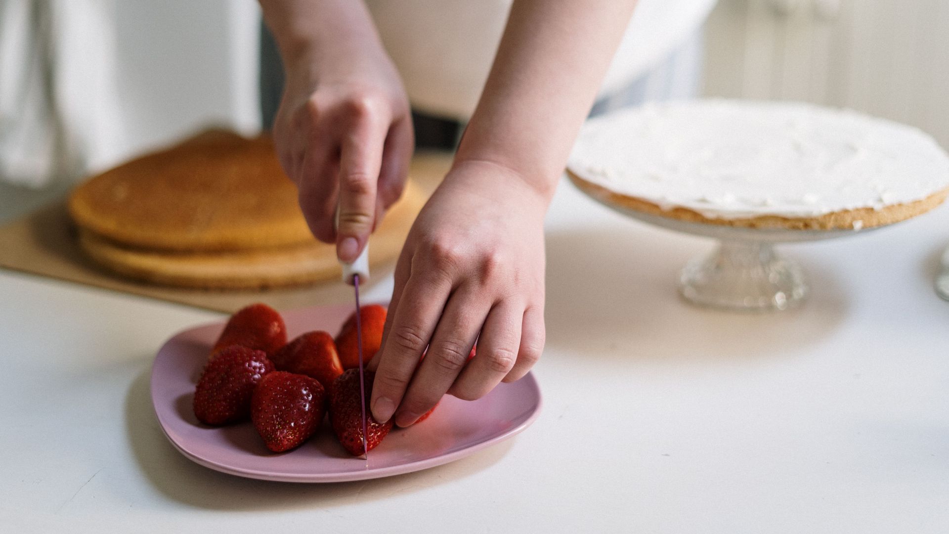 Hands slicing strawberries for a delicious homemade cake.